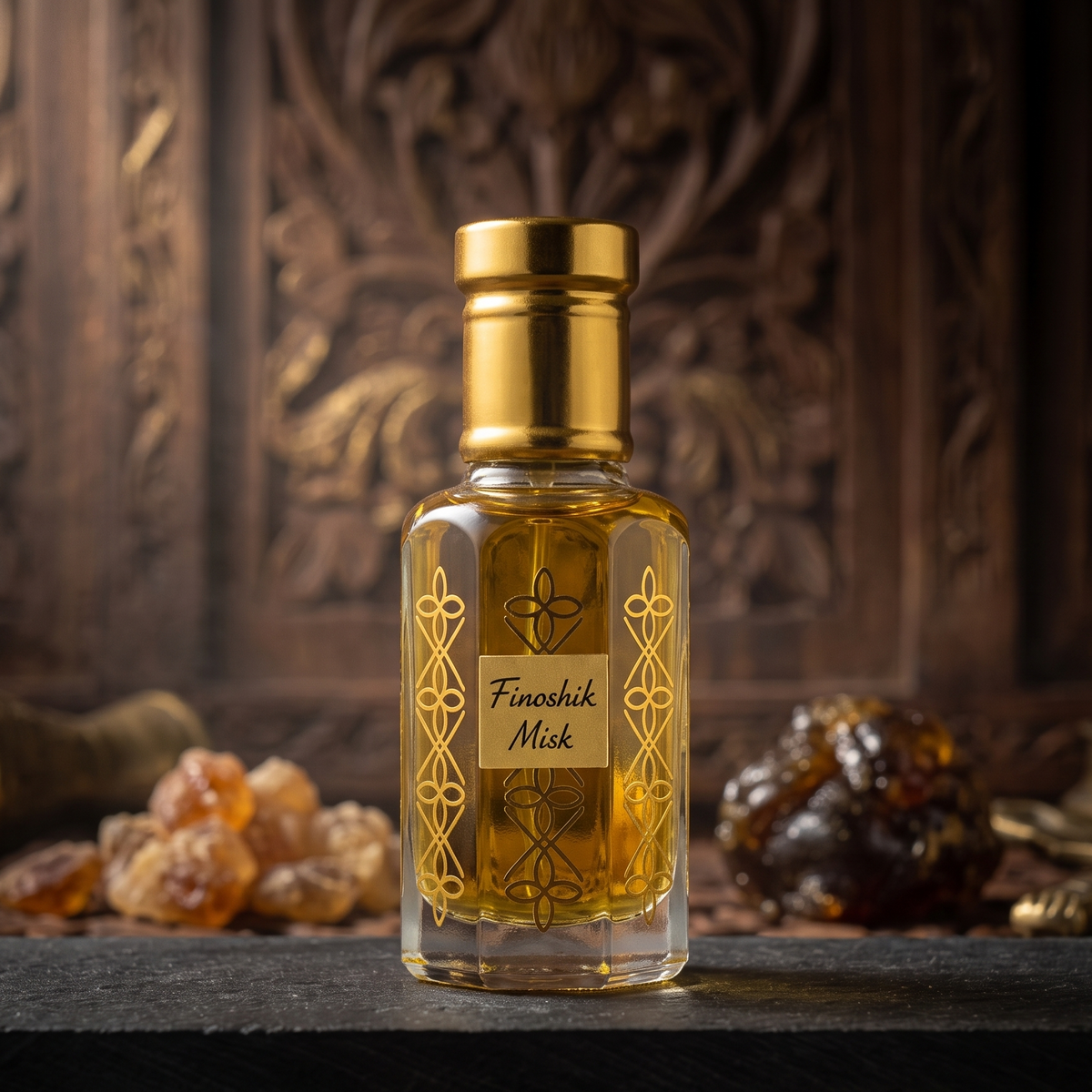 A small rectangular glass bottle of Finashik Misk perfume with a gold cap and gold decorative patterns, filled with amber-colored liquid, set on a dark stone slab with carved wood and amber stones in the background.
